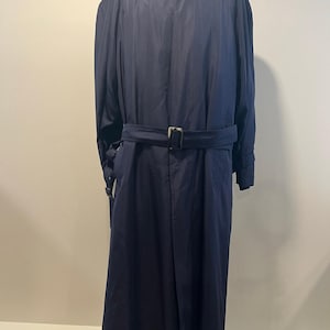 May include: A navy blue trench coat with a matching belt and buckle. The coat has a classic design with a collar and long sleeves. The coat is displayed on a mannequin.