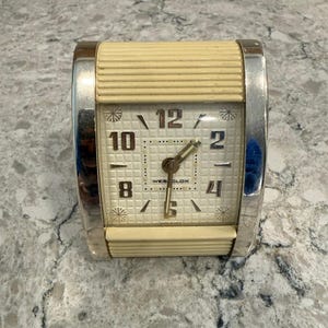 May include: A white ceramic mug with a black handle and the text "But First, Coffee" in a bold, black font. The mug is set against a blurred background, suggesting a cosy setting.