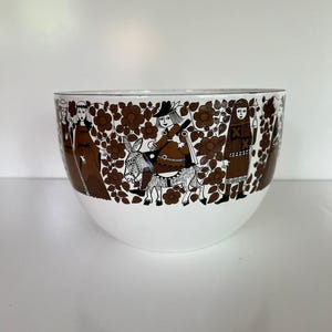 Puede incluir: Un cuenco de cerámica blanco y marrón con un patrón decorativo de figuras y flores. La parte superior del cuenco presenta un diseño repetido de figuras marrones y elementos florales sobre un fondo blanco. El cuenco tiene forma redonda.