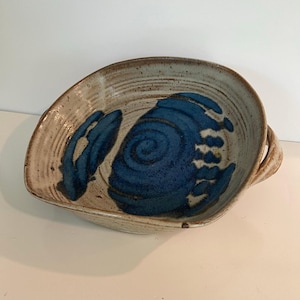 Puede incluir: Cuenco de cerámica hecho a mano con una forma orgánica única. El cuenco presenta un exterior moteado de color beige y un diseño azul vibrante y abstracto en el interior. Tiene dos asas pequeñas y es perfecto para servir o exhibir.