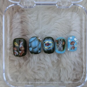 Pode incluir: Cinco unhas postiças em miniatura com diferentes desenhos de animais da floresta. As unhas são pintadas em tons de azul, verde e marrom. Uma unha apresenta uma raposa, outra uma joaninha, outra um coelho e duas apresentam cogumelos.