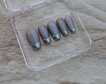 May include: Set of five iridescent press-on nails with silver metallic tips, displayed in a clear plastic case. The nails have a pearlescent finish with shades of pink, blue, and purple. The case is open, revealing the nail set on a soft, textured surface.