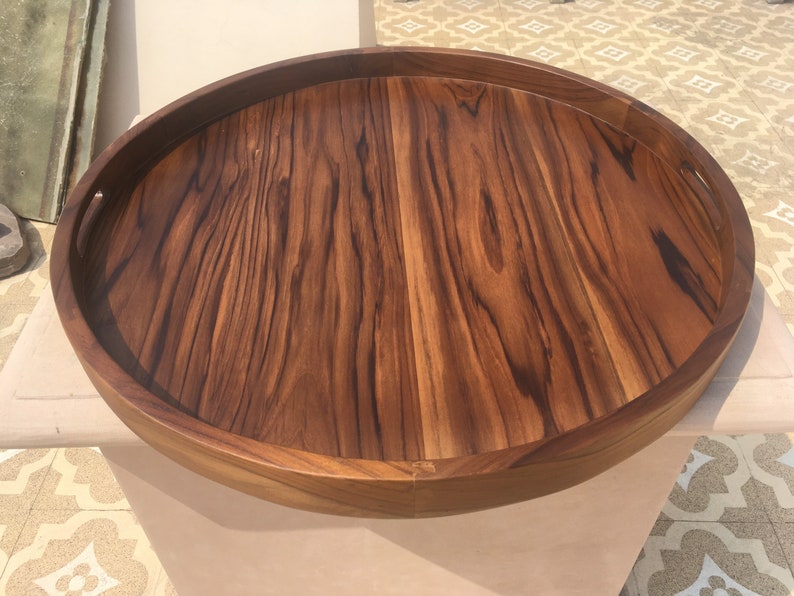 May include: A large, round wooden serving tray with a natural wood finish and a raised edge. The tray has two handles on the sides.