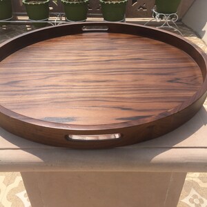May include: A large, oval wooden serving tray with two handles. The tray is made of dark wood with a rich grain pattern.