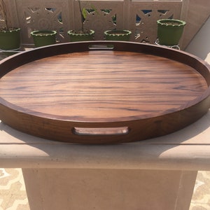 May include: A large, round wooden serving tray with two handles on the sides. The tray is made of dark brown wood with a natural wood grain pattern.