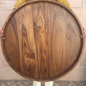 May include: A large, round wooden serving tray with a natural wood finish. The tray has a raised edge and is made of solid wood.