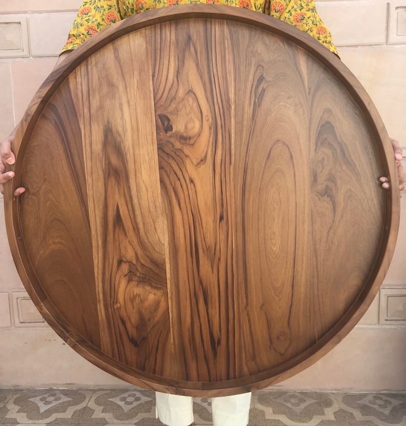 May include: A large, round wooden serving tray with a natural wood finish. The tray has a raised edge and is made of solid wood.