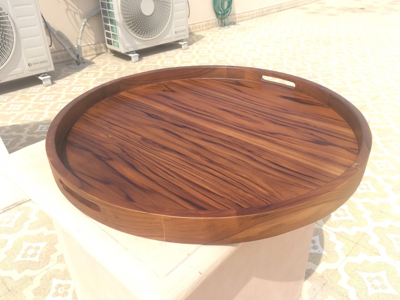May include: A large, round wooden serving tray with two handles. The tray is made of dark brown wood with a natural grain pattern.
