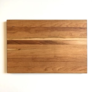 May include: A rectangular wooden chopping board with a natural wood grain finish. The board is made of cherry wood and has a smooth surface.