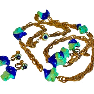 May include: A gold chain necklace with blue and green swirl-shaped glass beads. Matching clip-on earrings with blue and green swirl-shaped glass beads.