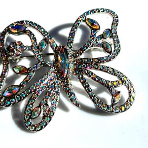 Peut inclure: Une broche en forme de papillon argentée avec des strass irisés. Le papillon a un design détaillé avec des ailes et un corps complexes.