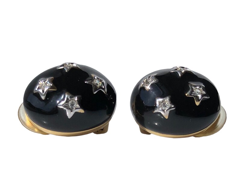 K&ouml;nnte beinhalten: Ein Paar schwarze Emaille-Clip-Ohrringe mit goldenen Akzenten und klaren Strass-Sternen.