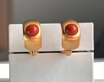 Könnte beinhalten: Ein Paar goldfarbene Ohrclips mit roten Korallen-Cabochons.