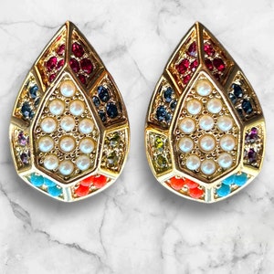 Könnte beinhalten: Ein Paar goldene tropfenförmige Ohrringe mit geometrischem Design. Die Ohrringe sind mit verschiedenen bunten Edelsteinen verziert, darunter rot, blau, grün und orange. Die Mitte jedes Ohrrings ist mit einem Cluster aus weißen Perlen gefüllt.