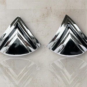 Peut inclure: Une paire de boucles d'oreilles géométriques triangulaires. Elles présentent une combinaison de noir et d'argent avec une finition brillante. Le design intègre des lignes angulaires, créant un look moderne et élégant. Accessoire de mode.
