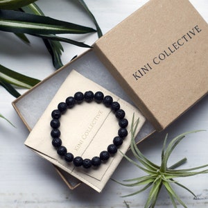 May include: A black lava rock beaded bracelet in a small cardboard box with the text "KINI COLLECTIVE" printed on the box.