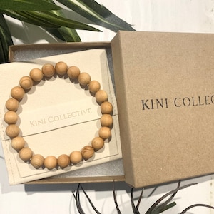 May include: A wooden bead bracelet in a small, beige box with the text "KINI COLLECTIVE" printed on the box and the inside of the box.