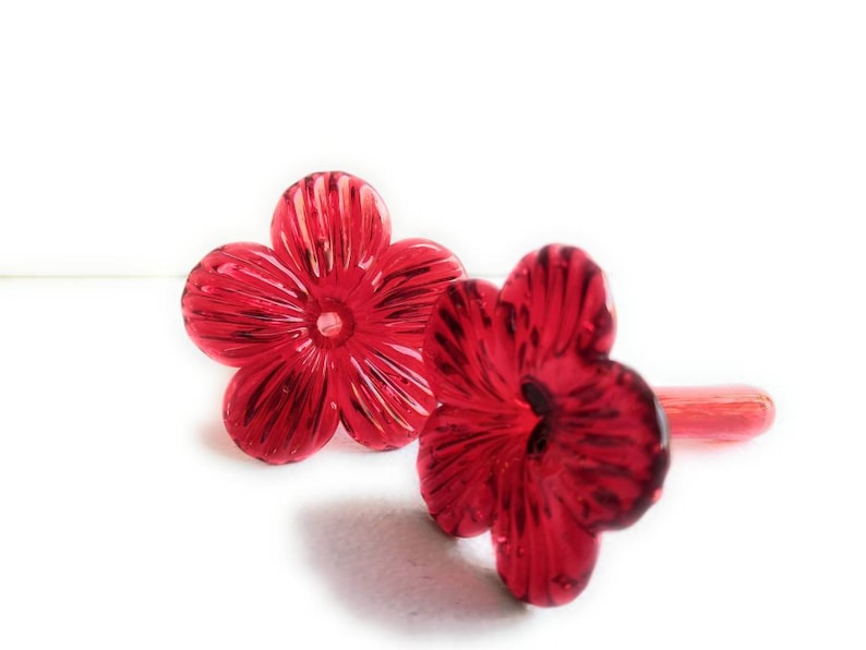 May include: Two red glass hummingbird feeders shaped like flowers. The feeders have a small opening at the top for filling with nectar.