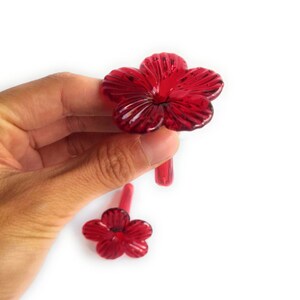 May include: Two red glass hummingbird feeders shaped like flowers with a long, thin stem.