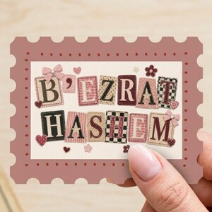 Op de afbeelding: Een rechthoekige kaart met een geschulpte rand in oudroze, met de tekst B'EZRAT HASHEM gespeld in individuele stofachtige patches. De letters zijn versierd met kleine hartjes, bloemen, strikjes en diverse patronen zoals vichy en ruitjes.