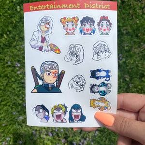 Może przedstawiać: Arkusz kolorowych naklejek z postaciami z anime. Naklejki przedstawiają r&oacute;żne postacie ze szczeg&oacute;łowymi wyrazami twarzy i strojami. Arkusz ma u g&oacute;ry napis "Entertainment District" w kolorze pomarańczowym i białym.