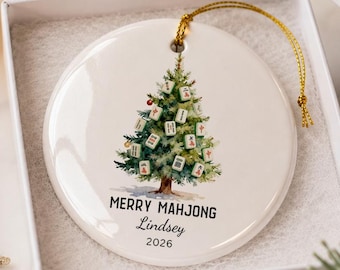May include: A round white ceramic ornament featuring a watercolor illustration of a Christmas tree decorated with Mahjong tiles. The text reads MERRY MAHJONG, the name Lindsey, and the year 2026. It includes a gold hanging string.