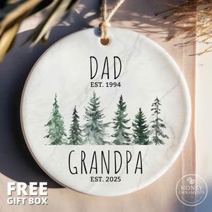 May include: White ceramic ornament with a marbleized design. The ornament features a watercolor illustration of a forest with green trees. The text "DAD EST. 1994" and "GRANDPA EST. 2025" is printed in black.