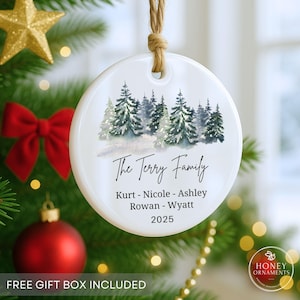May include: A round white ceramic ornament hanging from a jute twine loop. The front features a watercolor illustration of a snowy pine forest above the text The Terry Family, the names Kurt, Nicole, Ashley, Rowan, Wyatt, and the year 2025.