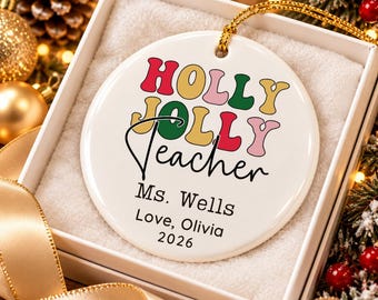 May include: A round white ceramic ornament with a gold hanging cord. The text reads HOLLY JOLLY in colorful retro-style letters, followed by the black script word Teacher, and the printed text Ms. Wells, Love, Olivia, and the year 2026.