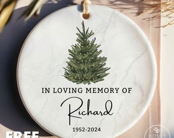 May include: A round white ceramic ornament with a marble texture, featuring a green watercolor Christmas tree illustration. The text reads IN LOVING MEMORY OF Richard 1952-2024. A jute twine string is attached to the top for hanging purposes.