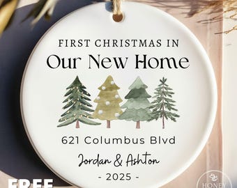 May include: A white ceramic Christmas ornament with a string for hanging. The ornament features the text "FIRST CHRISTMAS IN Our New Home" and a watercolor illustration of four Christmas trees. Below the trees are the address, names, and year.