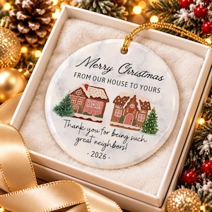 May include: A round white ceramic ornament with a marble texture featuring two gingerbread houses, two pine trees, and the text Merry Christmas FROM OUR HOUSE TO YOURS Thank you for being such great neighbors! - 2026 - with a gold hanging cord.