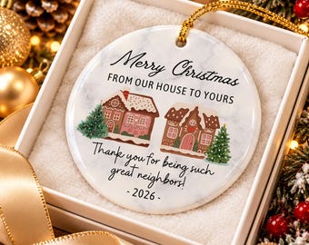 May include: A round white ceramic ornament with a marble texture featuring two gingerbread houses, two pine trees, and the text Merry Christmas FROM OUR HOUSE TO YOURS Thank you for being such great neighbors! - 2026 - with a gold hanging cord.