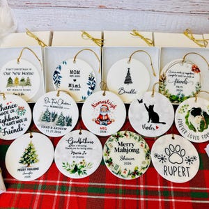 a collection of 12 ornaments, each with a unique design and inscription, arranged on a red and green plaid tablecloth.