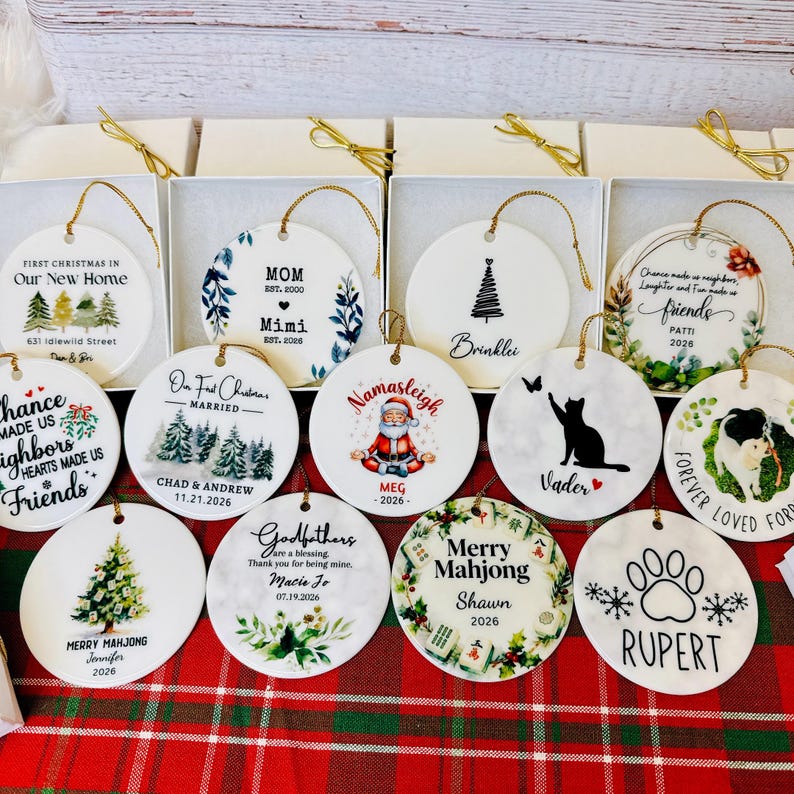 a collection of 12 ornaments, each with a unique design and inscription, arranged on a red and green plaid tablecloth.