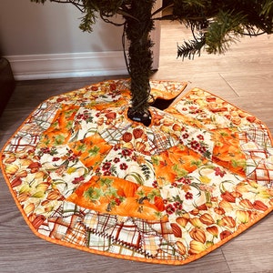 Op de afbeelding: Een boomrok in patchwork-stijl met een herfstthema. De rok is gemaakt van verschillende stoffen met een pompoen- en bloemenpatroon in tinten oranje, geel en groen. De rok heeft een bruine zoom.