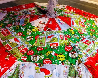 May include: A colorful Christmas tree skirt featuring a patchwork design with red, green, and white panels. The skirt showcases Grinch-themed illustrations, Christmas trees, and snowflakes. The border is trimmed with a red and white striped pattern.