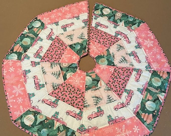 Könnte beinhalten: Ein Weihnachtsbaumrock mit einem rosa-grünen Feiertags-Thema. Der Rock hat ein Patchwork-Design mit rosa Lastwagen, die Geschenke, Schneeflocken und Weihnachtsschmuck transportieren. Der Rock hat einen Durchmesser von etwa 102 cm.