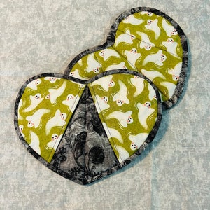 May include: Two heart-shaped pot holders with a green and white ghost print and a black and white floral print.