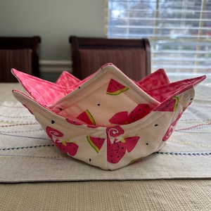 May include: A pink and white fabric bowl with a watermelon print. The bowl is folded and has a star shape.