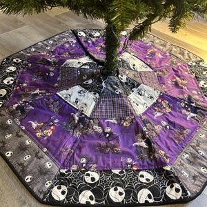 May include: Octagonal Christmas tree skirt featuring a patchwork design with a purple and black color scheme. The skirt has a border with white skull and spiderweb patterns. The center features images of characters from The Nightmare Before Christmas.