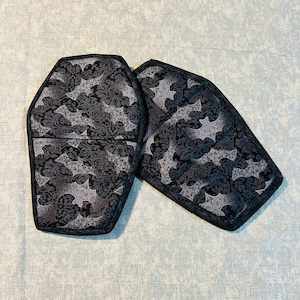 May include: Two black and white coffin-shaped pot holders with a bat pattern.