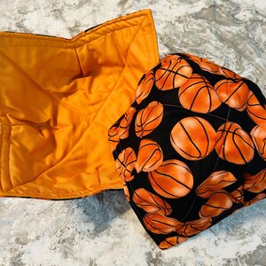 May include: Two bowl cozies. One is orange, the other is black with orange basketballs. The orange cozy is quilted and has a black border. The basketball cozy is also quilted and has a black border.