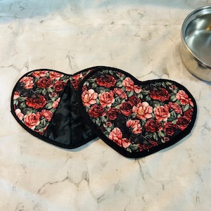 May include: Two heart-shaped pot holders with a black trim and a floral pattern featuring red roses on a black background.