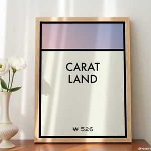 May include: A framed print with a light pink and blue gradient background. The text "CARAT LAND" is in black text on a white background. The bottom of the print has the text "₩ 526" in black text.