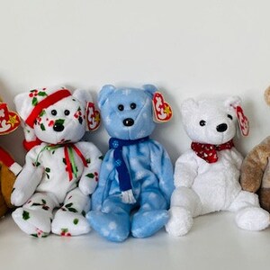May include: Five plush beanie baby bears in various colors and patterns. The bears are wearing holiday-themed accessories, including a Santa hat, a scarf, and a holly-patterned hat.