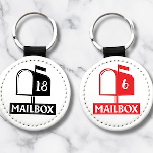 May include: Two white round keychains with black key rings. Each keychain has a black and white mailbox with a number on it. One mailbox has the number 18 and the other has the number 6. Both keychains have the word "MAILBOX" printed on them.