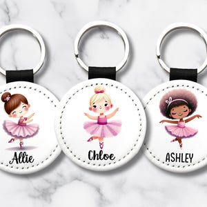 May include: Three round keychains with illustrations of ballerinas in pink tutus. Each keychain features a different ballerina with a unique hairstyle and skin tone. The names "Allie", "Chloe", and "Ashley" are printed below each ballerina.