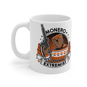 May include: White ceramic coffee mug with a black and orange graphic of a bear wearing a bandana and holding a rifle. The graphic is surrounded by a black circle with the text "MONERO EXTREMIST" in white.