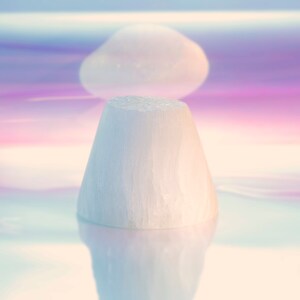 Puede incluir: Un objeto blanco en forma de cono se encuentra sobre una superficie iridiscente. La superficie tiene un degradado de colores rosa, azul y morado.